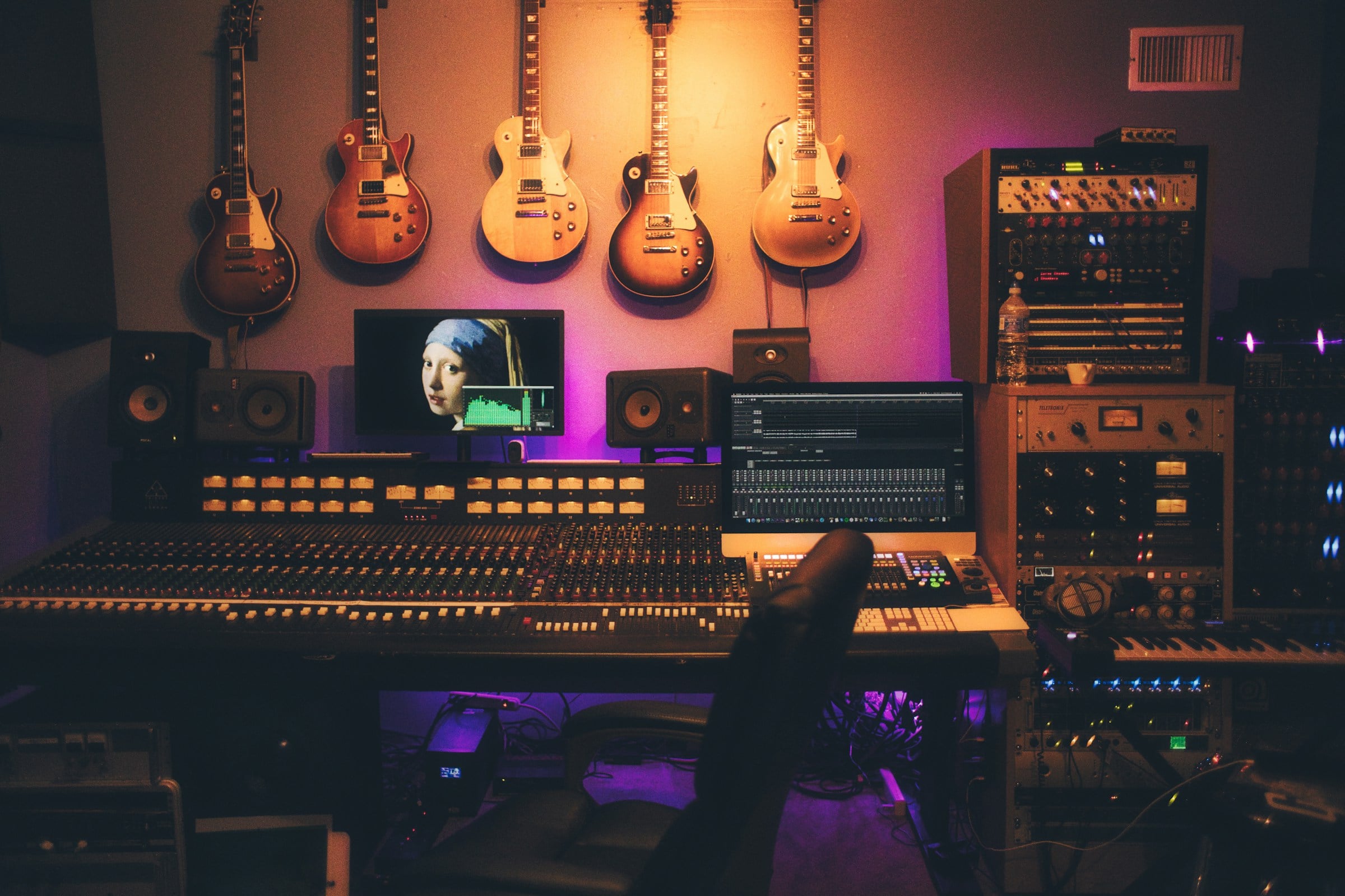 Music studio mixing console with electric guitars on the wall, lit by warm tungsten light